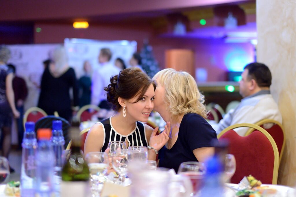 2 ladies whispering to each other at an embarrassing corporate holiday party