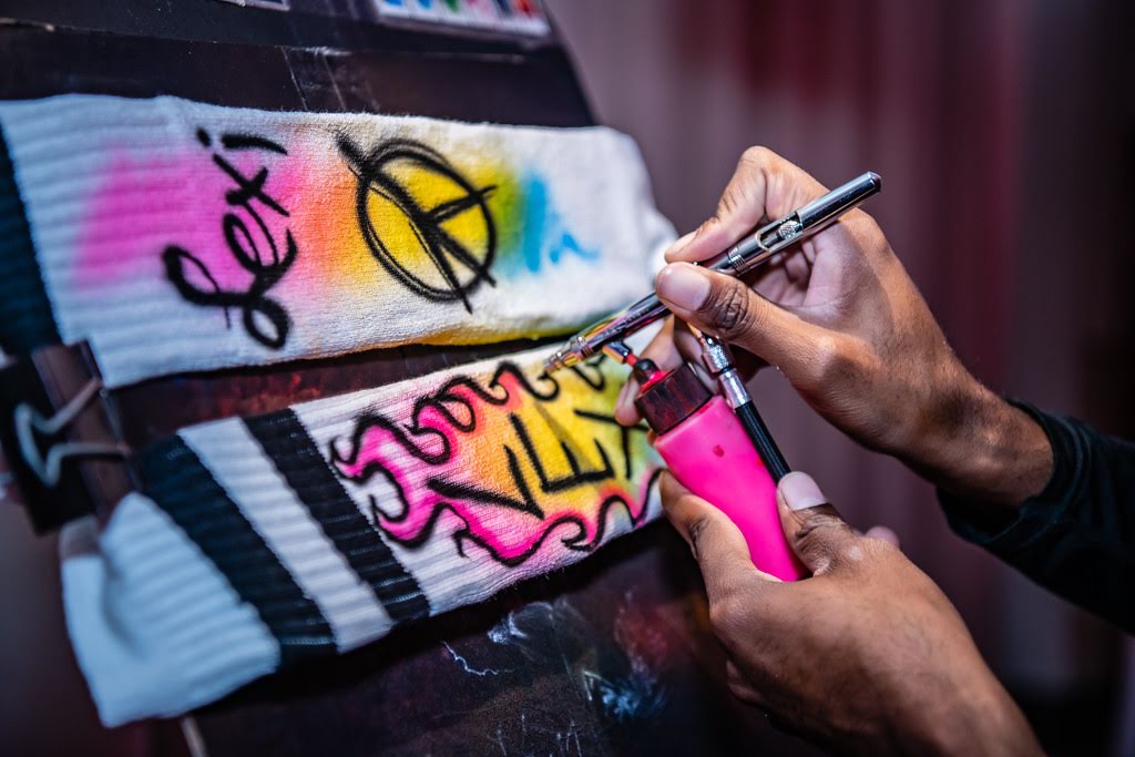 An artist uses an airbrush gun to brightly paint white socks on an easel