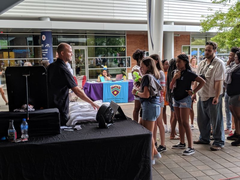 An airbrush artists stands at a black table with a line of people waiting to place an order.