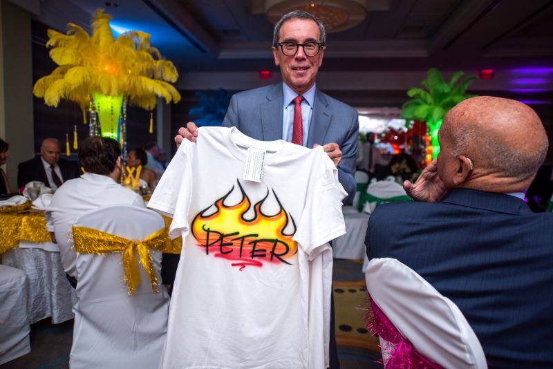 A man stands up holding his airbrushed t-shirt with the name 'Peter' painted on it.