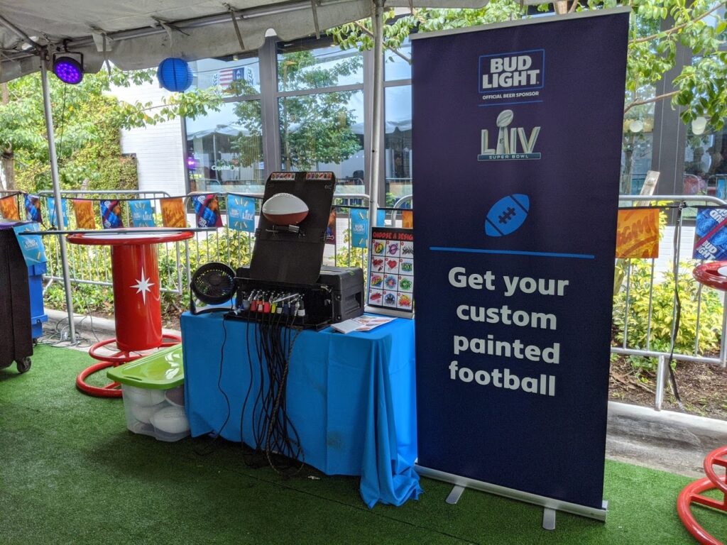Airbrush Events booth with a banner advertising custom painted footballs during Bud Light activation