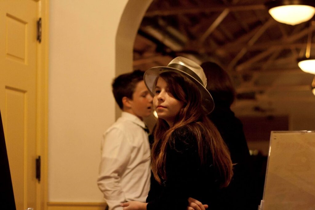 a dark-haired girl wearing a party hat stands in the midst of people