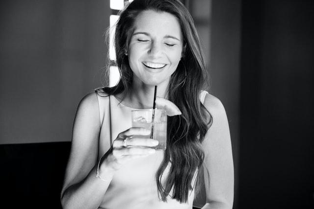 a smiling woman with a cocktail at the virtual cocktail party