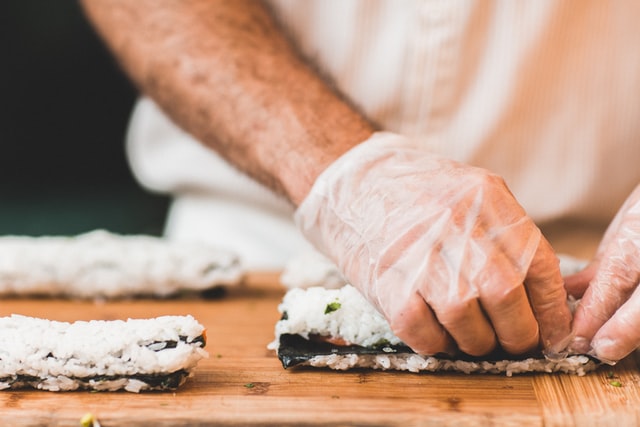 A latex gloved hand prepares sushi