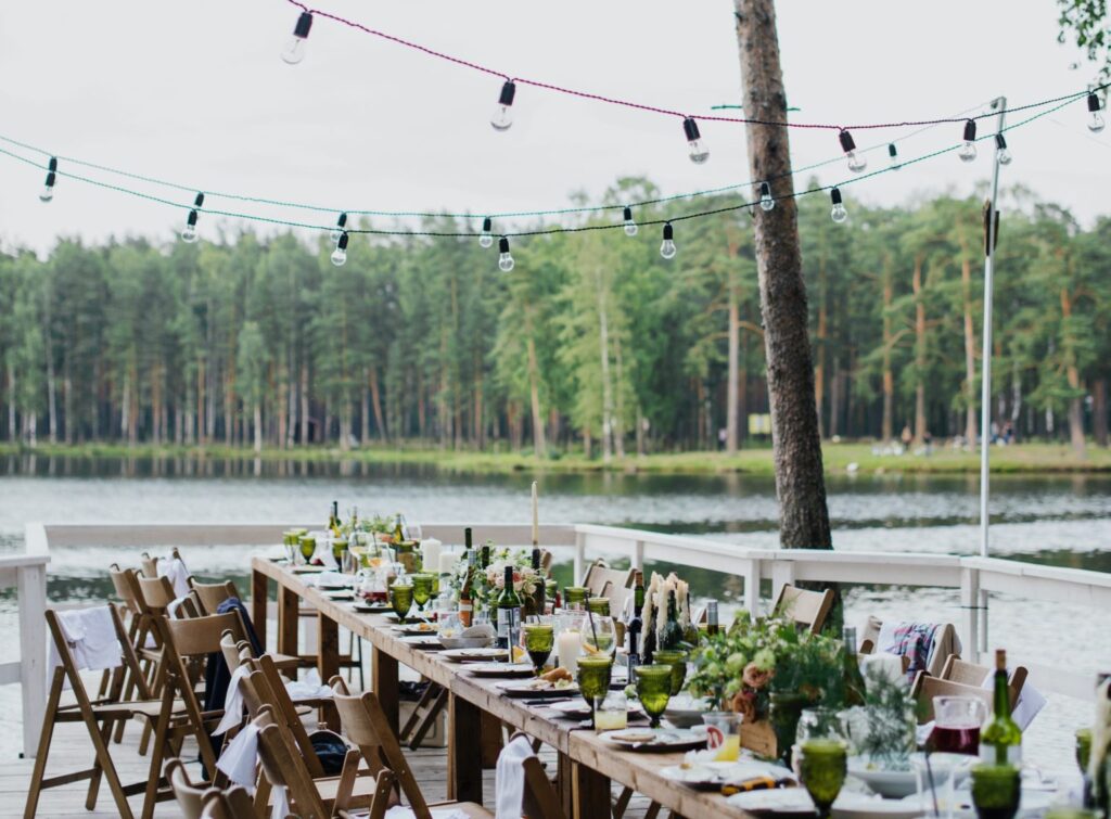 a long wooden table decorated with plants and dishes set in front of a pond