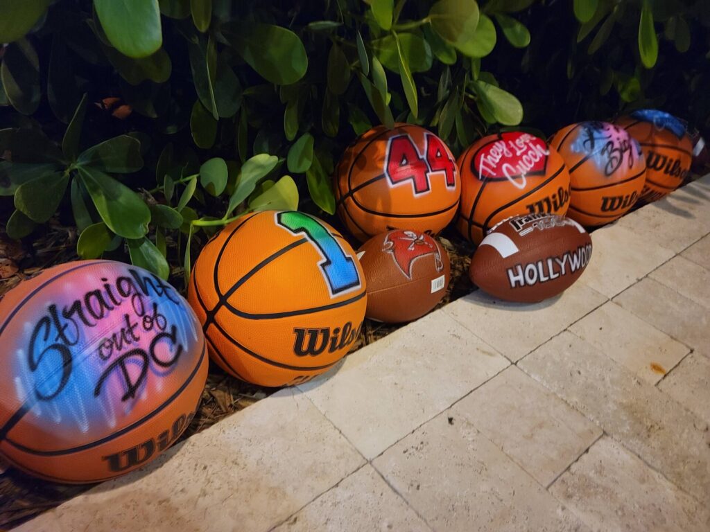 Brightly painted basketballs lined up under a tree. They are personalized as party favors for bar mitzvahs