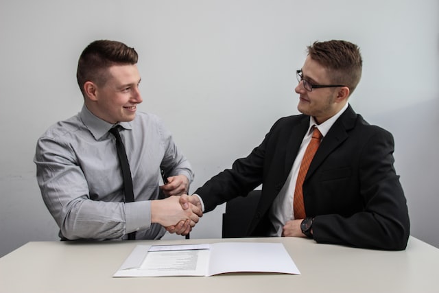 2 men shake hands while sitting at a white table with contract in front of them - Breaking Into Corporate Event Planning: A Beginner's Guide to Finding Your Niche