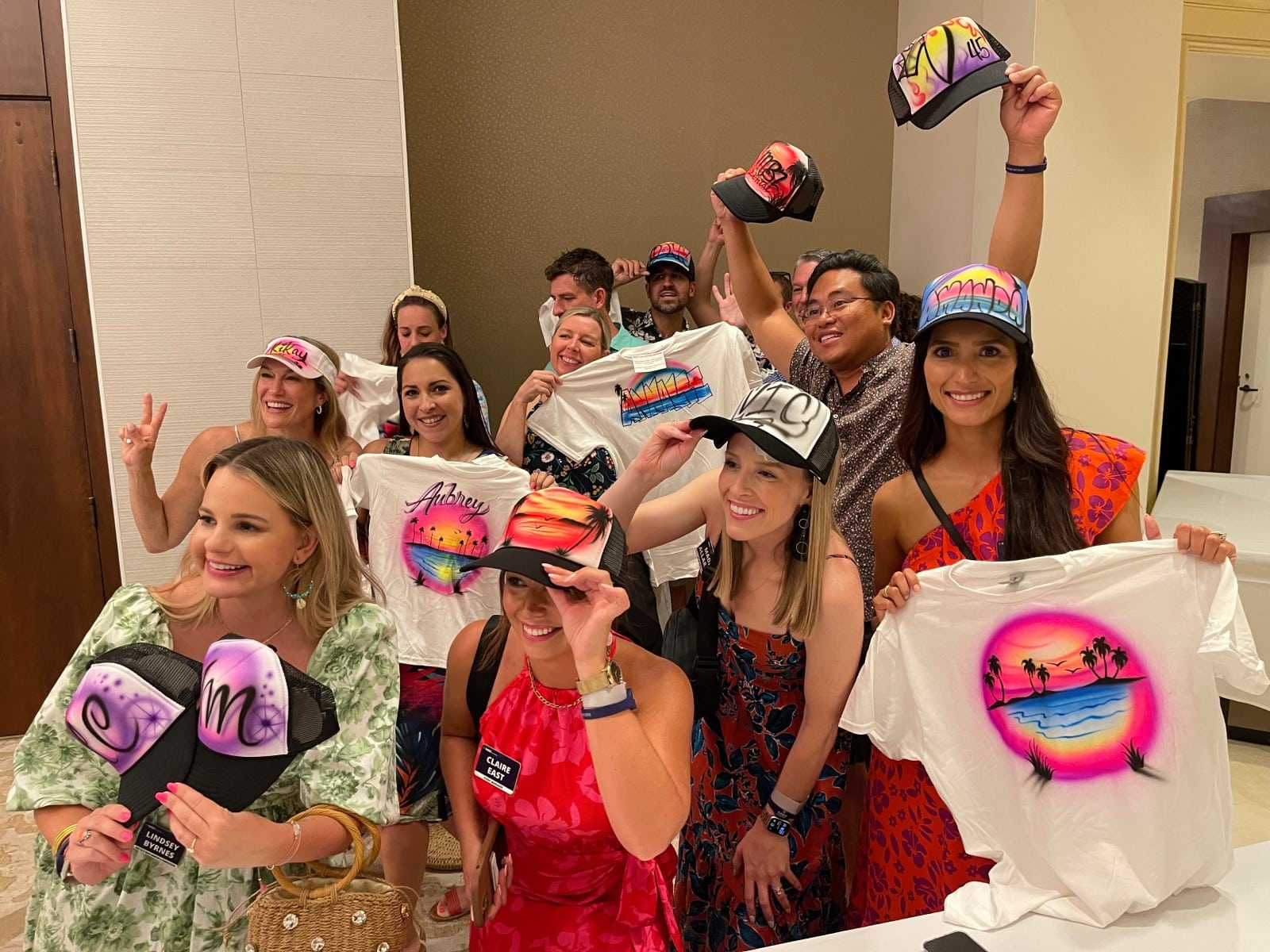 A group of event guests smile for the camera while showing off their airbrushed t-shirts and hats - corporate event planning