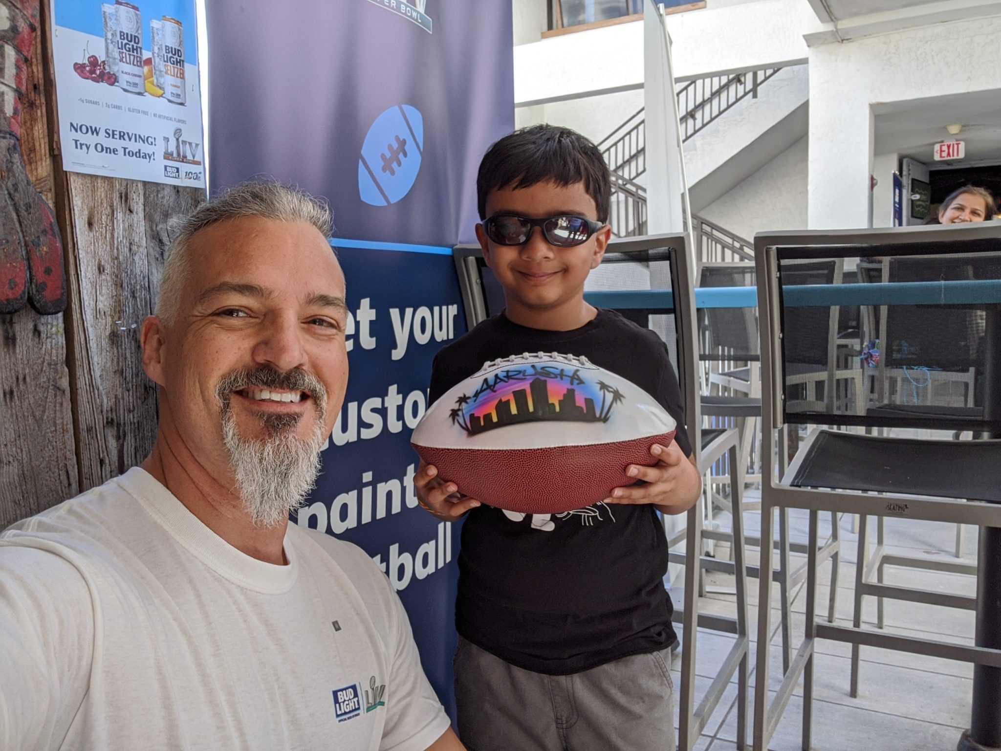 Pete poses with a young boy holding a football that has fresh airbrush paint on it.