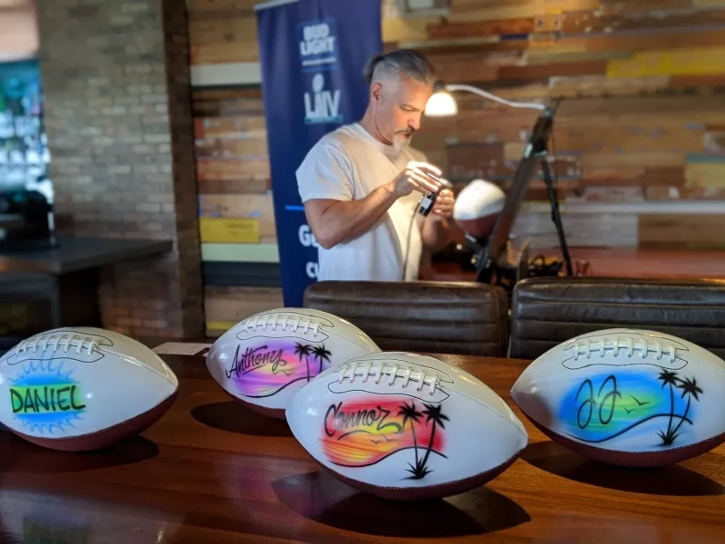 Personalized footballs sit on a wooden table in front of artist at brand activations